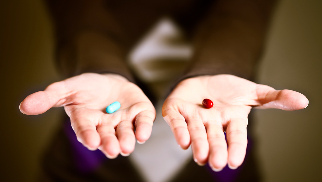 I den ena handflatan finns en blå läkemedelskapsel och i den andra en röd läkemedelskapsel.